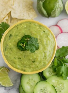 Bowl of Roasted Tomatillo Avocado Salsa surrounded by chips and veggies