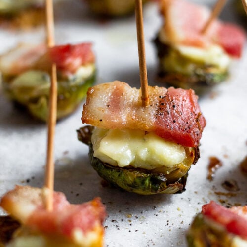 Individual crispy brussel sprouts with bacon and cheese with a toothpick stuck in each one.