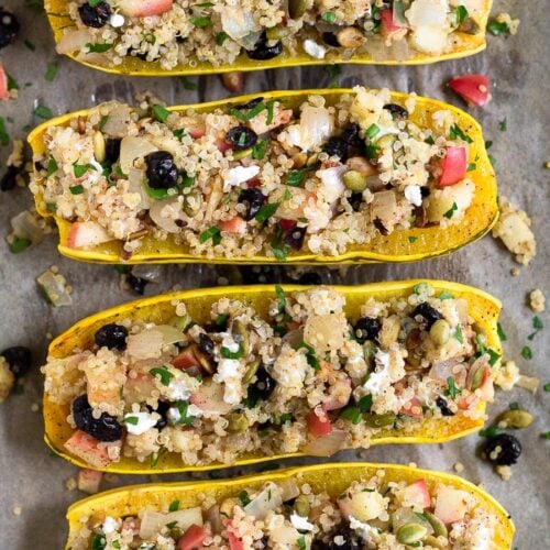 Stuffed delicata squash with quinoa, apple, goat cheese, cranberries, and pumpkin seeds, They are sitting on a baking sheet with some filling that has