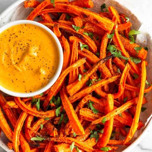 Overhead shot of carrot fries in a bowl topped with cilantro. In the bowl is a small ramekin with curry dipping sauce.