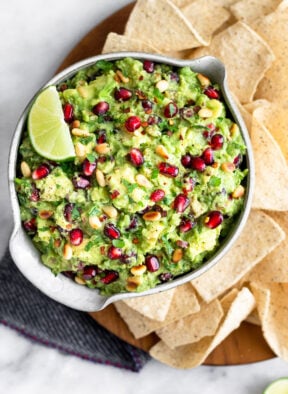 Large plate filled with chips and a bowl of pomegranate guacamole topped with a lime wedge.