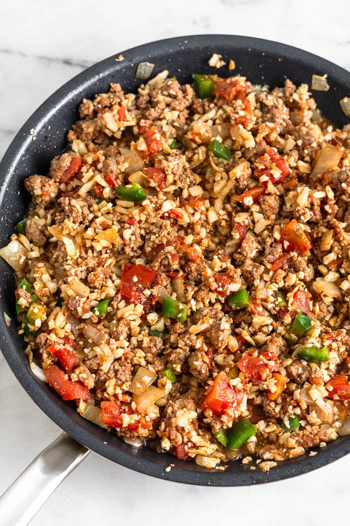 Pan filled with cooked ground beef, cauliflower rice, onion, jalapeno, canned tomatoes, and spices.