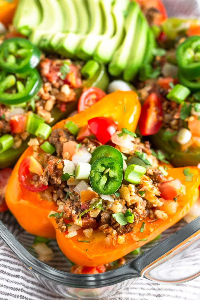 Close up of a Whole30 stuffed pepper topped with beef and cauliflower rice. It is topped with jalapeno, cilantro, and green onion. Surrounding it is more stuffed peppers in a glass baking dish.