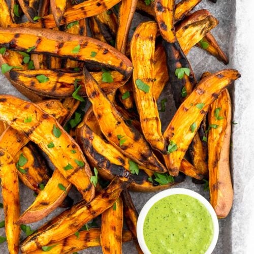Baking sheet with grilled sweet potato fries topped with fresh parsley an a green dipping sauce.