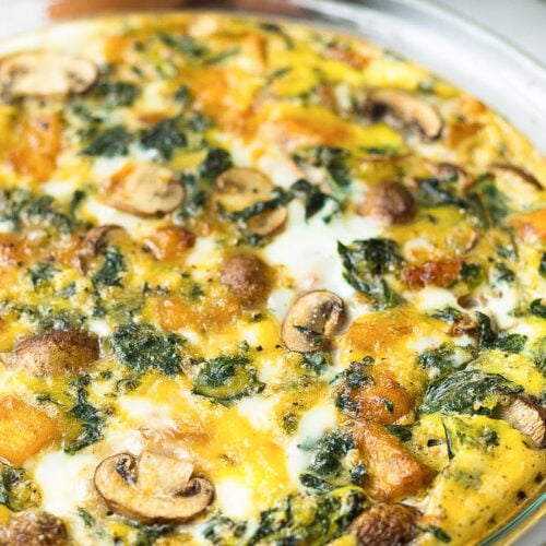 Crustless pumpkin quiche in a pie pan with eggs, pumpkin, and kale behind it.