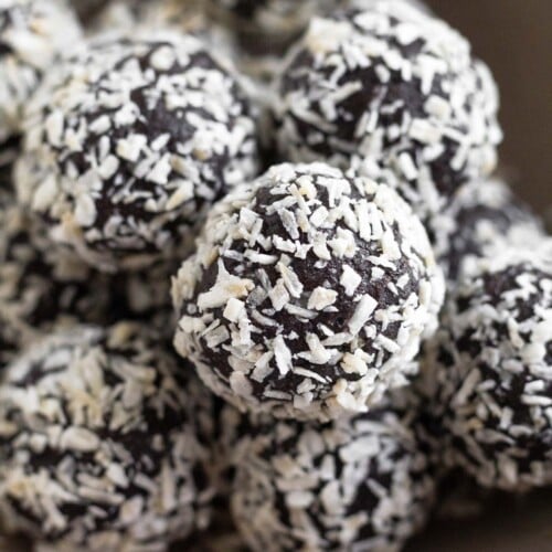 A pile of chocolate peppermint energy balls in a small brown bowl. They are coated with shredded coconut.