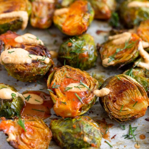 A bunch of buffalo brusssel sprouts topped with cheesy buffalo sauce and fresh dill on a baking sheet.