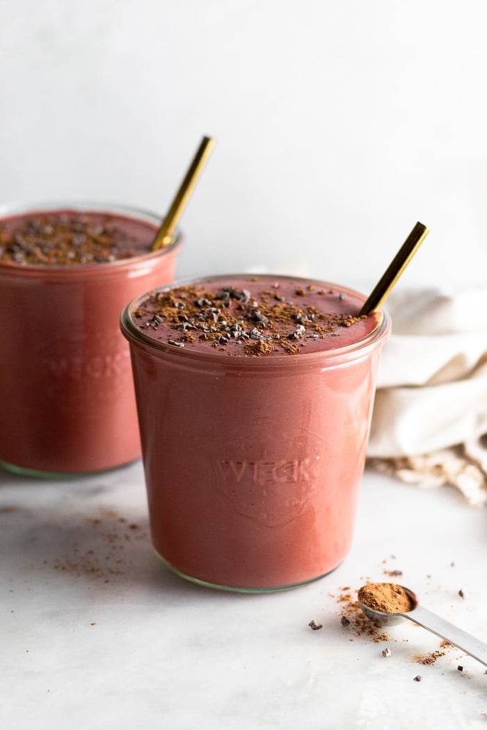 Batido de alta proteína con remolacha, yogur griego y chocolate en dos tarros con pajitas que salen de ellos.