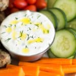 Close up of a bowl of tzatziki sauce with fresh raw veggies around it