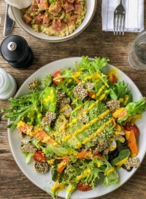Salad topped with fresh veggies, avocado, and a turmeric tahini dressing