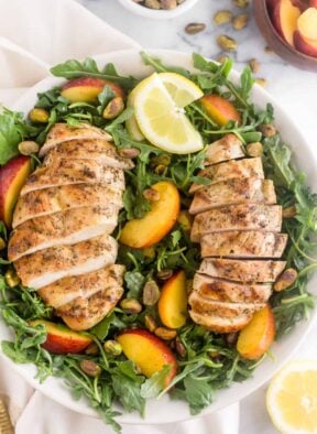 Large white bowl filled with a Peach and Pistachio Salad with Grilled Chicken on top of a white linen
