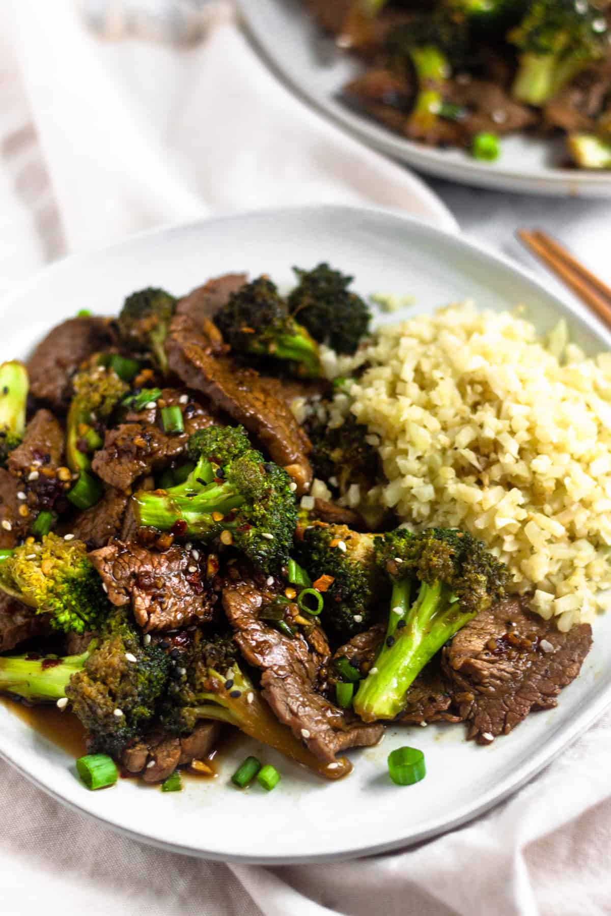 White plate filled with paleo beef & broccoli and cauliflower rice, topped with sesame seeds