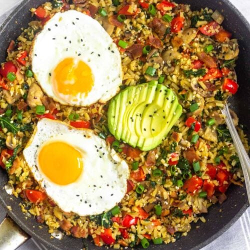 Large saute pan filled with whole30 and paleo breakfast fried rice topped with two fried eggs, sliced avocado, and sesame seeds