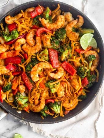 A large sauté pan with Whole30 Shrimp & Butternut Squash Noodles with Curry Peanut Sauce garnished with two lime wedges