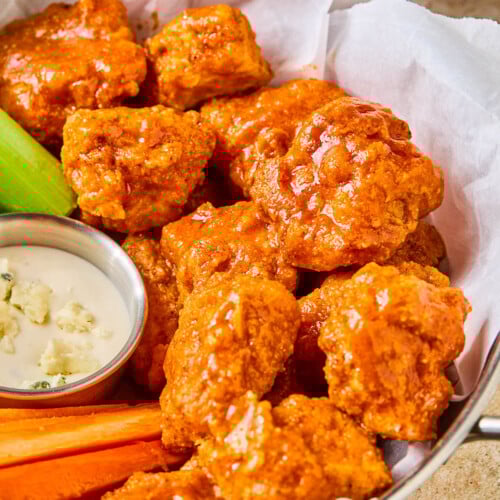 Air fryer boneless buffalo wings in a basket with carrot sticks, celery sticks, and a small ramekin of blue cheese dressing.