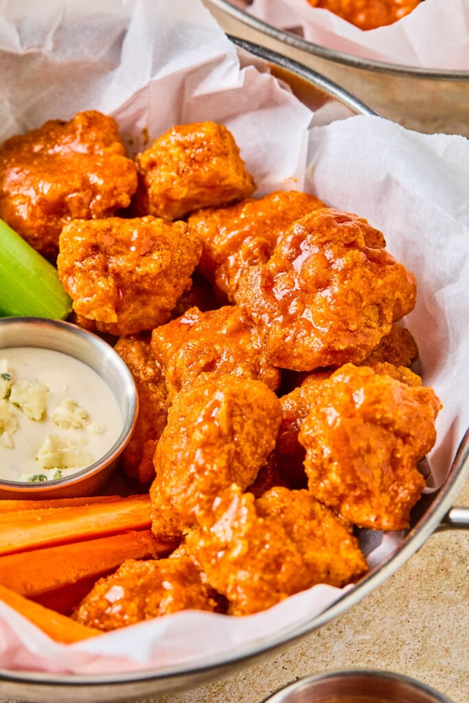 Air fryer boneless buffalo wings in a basket with carrot sticks, celery sticks, and a small ramekin of blue cheese dressing.