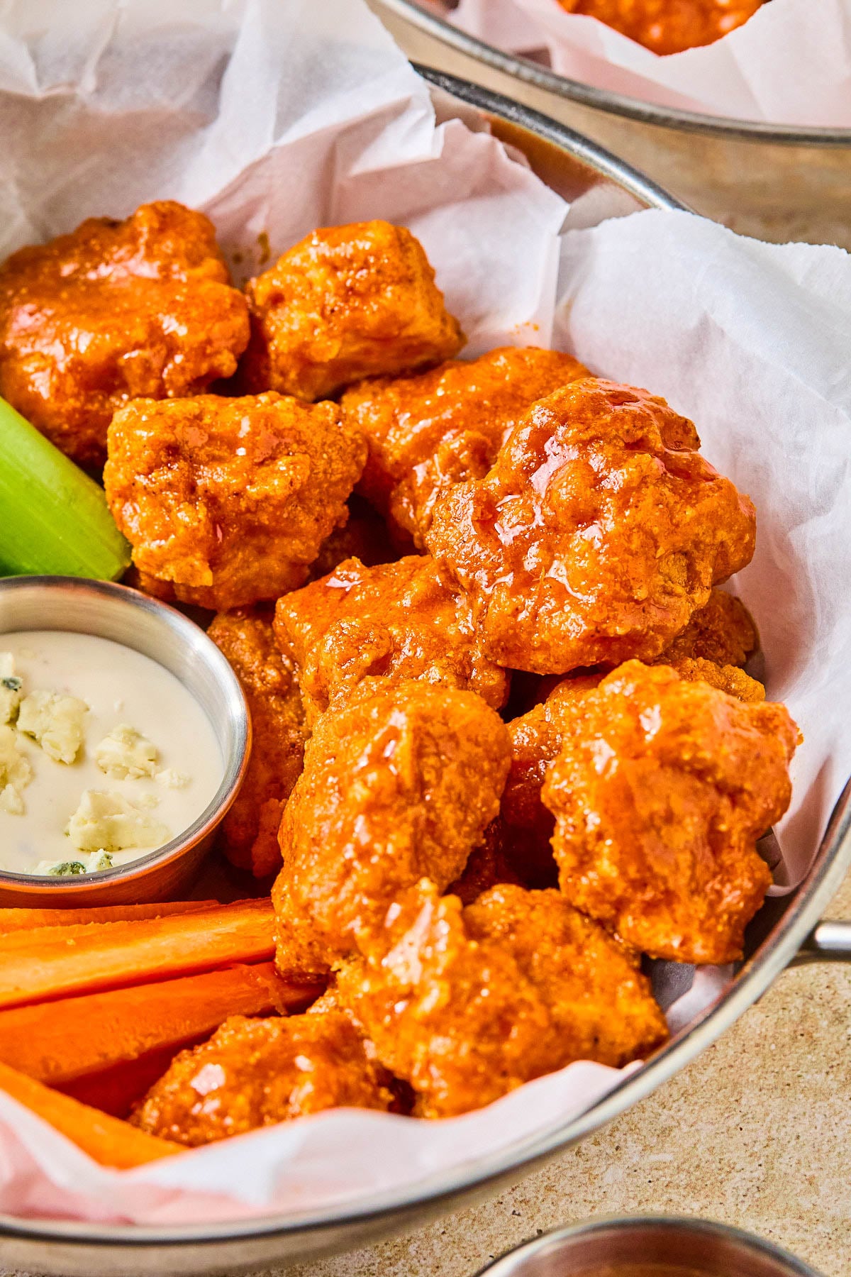 Air fryer boneless buffalo wings in a basket with carrot sticks, celery sticks, and a small ramekin of blue cheese dressing.