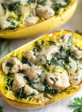Spaghetti squash boat stuffed with chicken Caesar salad. Another stuffed spaghetti squash is behind it and a few sprigs of parsley are around it.