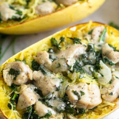 Spaghetti squash boat stuffed with chicken Caesar salad. Another stuffed spaghetti squash is behind it and a few sprigs of parsley are around it.