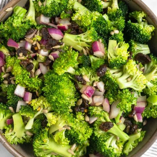 Healthy broccoli salad with raisins and sunflower seeds in a large bowl. The bowl is on a striped kitchen towel.