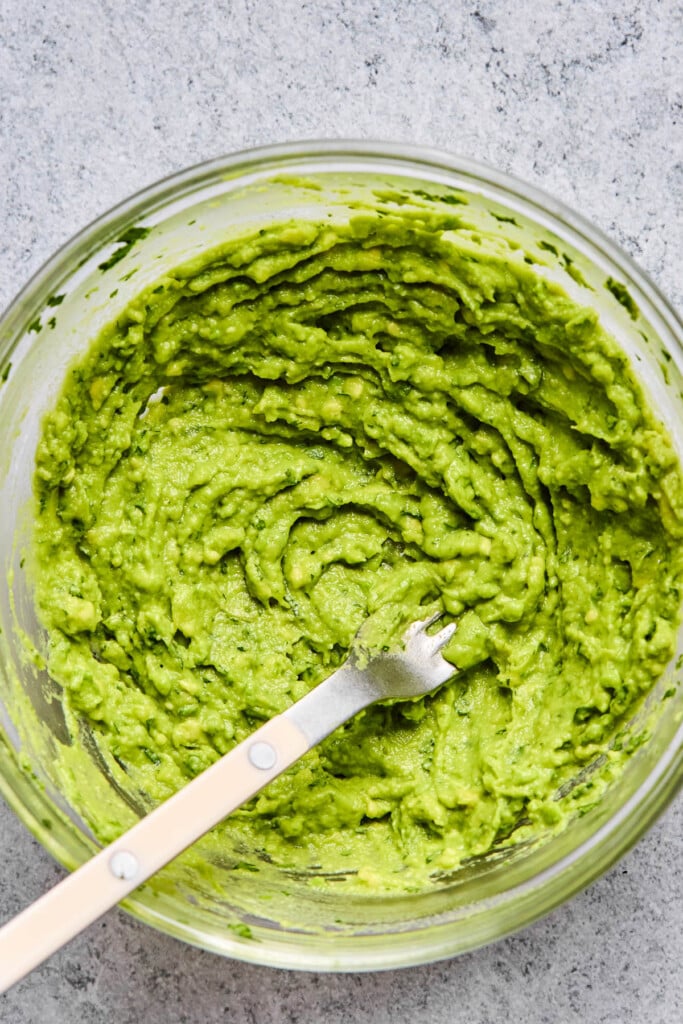 A glass bowl filled with guacamole with a fork in it.