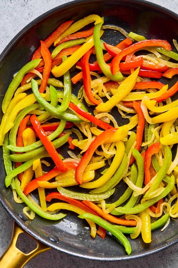 Large skillet with saut&eacute;ed sliced onions and peppers in it.