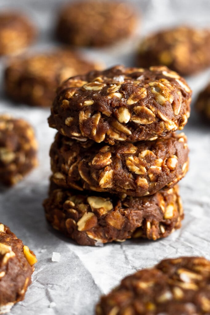 Three protein no bake oatmeal cookies stacked on top of each other. Around the stack of cookies are more cookies