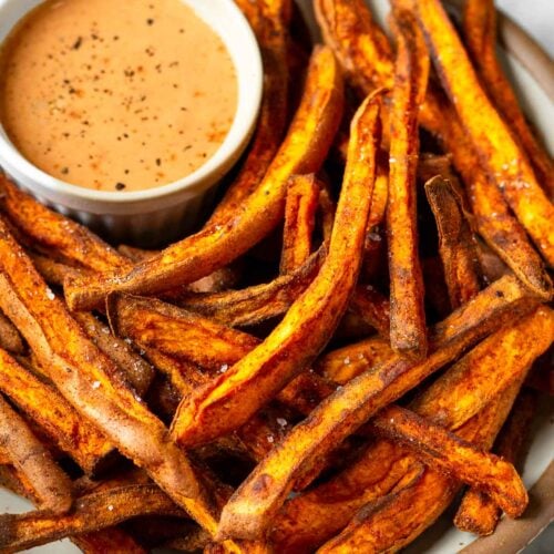 Air fryer sweet potato fries on a plate with a ramekin of dipping sauce.