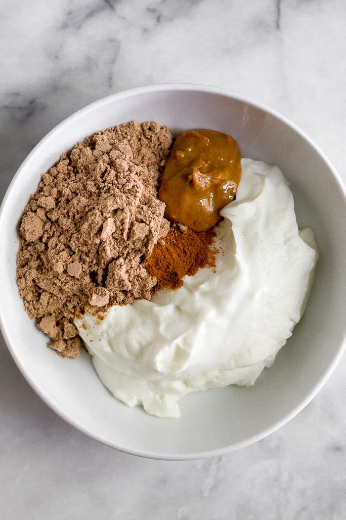 Tazón blanco relleno de yogur, proteína de chocolate en polvo, mantequilla de cacahuete y canela