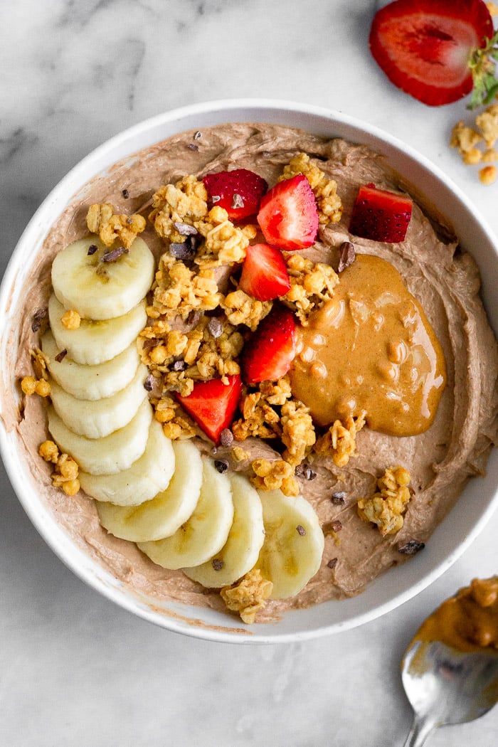 Bowl de petit-déjeuner au yaourt garni de banane, granola, fraises, beurre de cacahuète et miel.