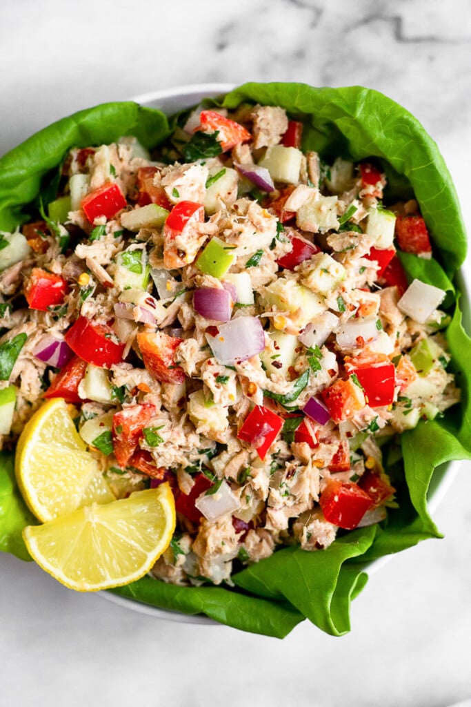 Healthy tuna salad on top of some leaves of bib lettuce in a bowl. It is garnished with lemon slices.