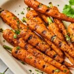 Grilled carrots on a serving platter topped with chopped cilantro. Around the platter is more fresh cilantro.