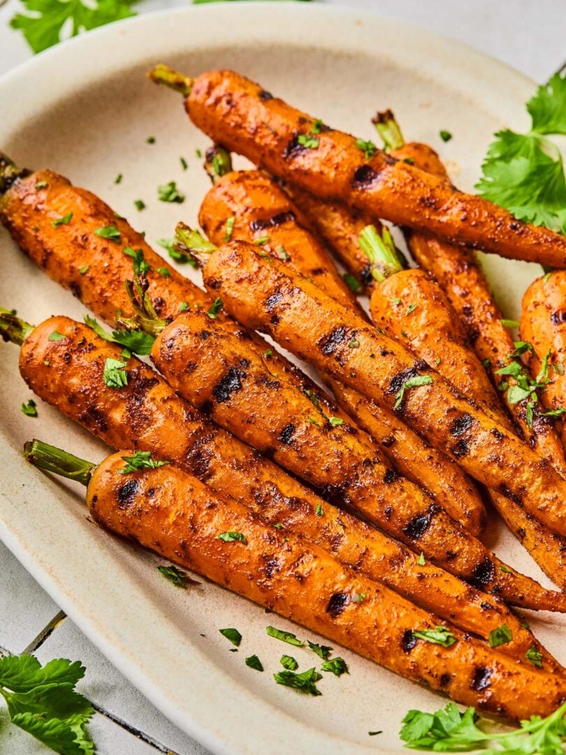 Grilled carrots on a serving platter topped with chopped cilantro. Around the platter is more fresh cilantro.