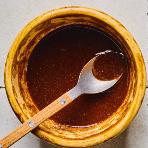 A small bowl of spices and oil mixed together with a spoon in it.