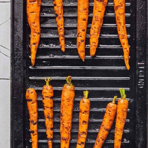 Overhead shot of carrots on the grill. The carrots are being cooked and have grill marks on them.