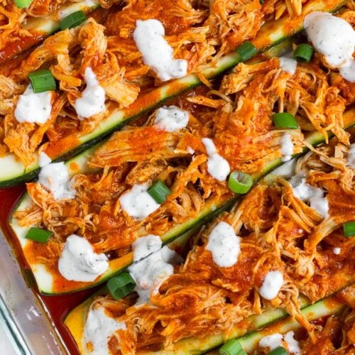 Close up of buffalo chicken zucchini boats topped with blue cheese dressing and green onions.