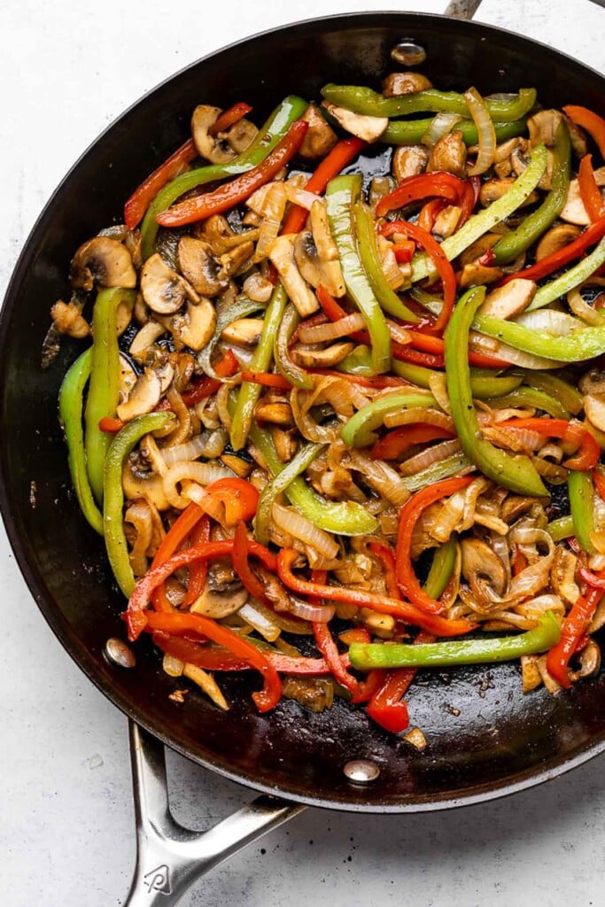 Large skillet filled with saut&eacute;ed onions, peppers, and mushrooms.