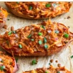 Twice baked BBQ chicken stuffed sweet potatoes on a baking sheet. They are garnished with more BBQ sauce and chopped green onions.