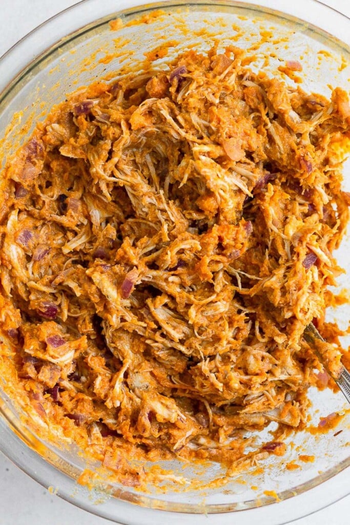 Large glass bowl filled with shredded chicken mixed with cooked mashed sweet potato, saut&eacute;ed onions, and spices.