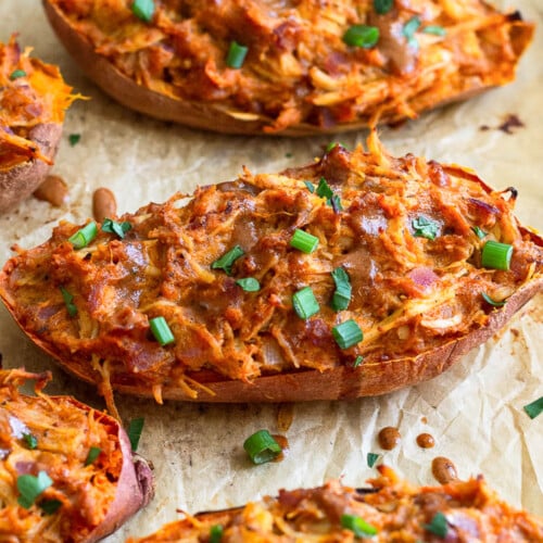 Twice baked BBQ chicken stuffed sweet potatoes on a baking sheet. They are garnished with more BBQ sauce and chopped green onions.