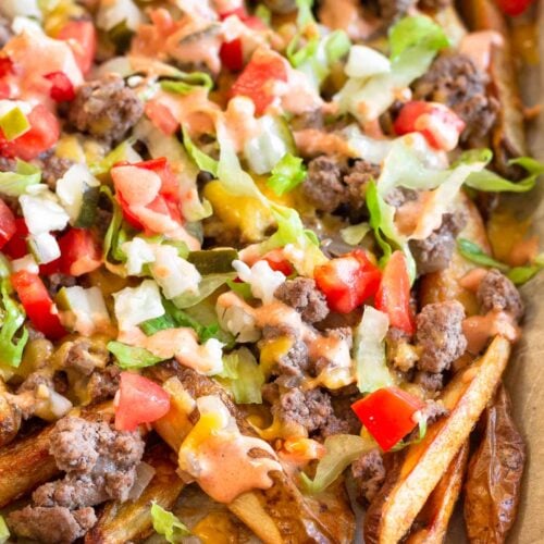 Cheeseburger fries on a large baking sheet topped with lettuce, tomato, pickles, and special sauce.