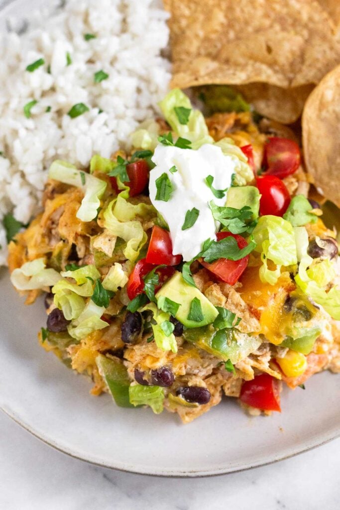A close up of a piece of chicken taco casserole on a plate with tortilla chips and rice.