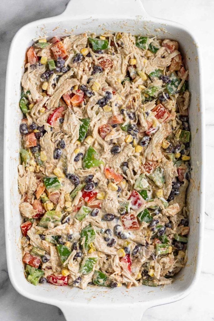 Baking dish with a mixture of shredded chicken, veggies, black beans, corn, spices, salsa, and greek yogurt before it is baked.