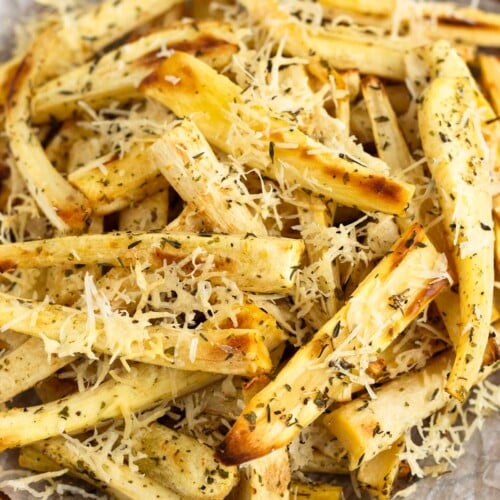 Roasted parsnips with crispy parmesan cheese and herbs on parchment paper on a wooden plate.