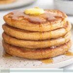 A plate of four cottage cheese pancakes topped with butter and syrup. There are some fresh berries on the plate. Behind the plate is a bowl of more berries and another stack of pancakes.