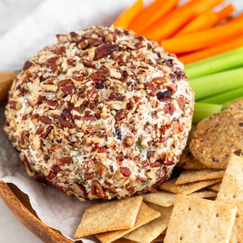 Pineapple cheese ball coated in chopped nuts on a dish surrounded by crackers, celery sticks, and carrots sticks.