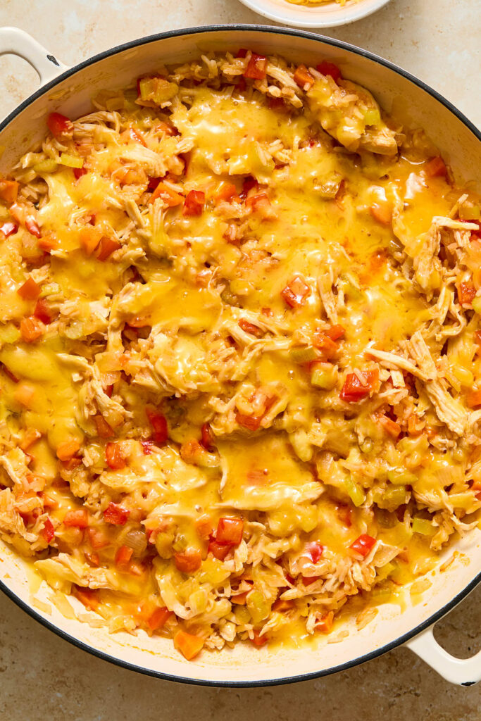 Large white enameled skillet filled with a cooked mixture of shredded chicken, white rice, and veggies topped with melted cheese.