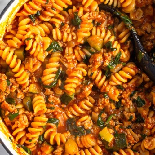 Large white dutch oven filled with ground turkey pasta with veggies. A spoon is also in the pot.