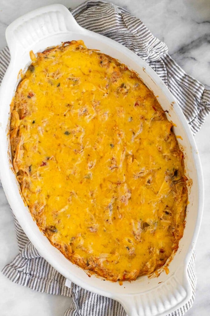 Chicken cheese dip in a white baking dish on a striped kitchen towel.