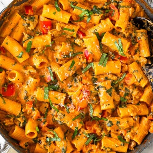 Cottage cheese pasta with ground turkey and veggies in a large skillet garnished with basil and parmesan cheese. The skillet is on top of a striped towel.